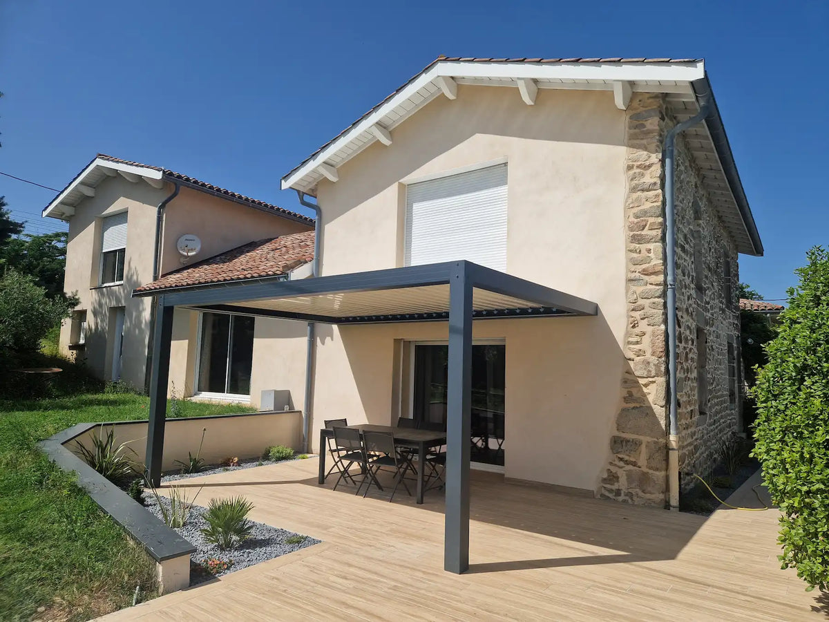 pergola en aluminium à lames orientables installée contre la façade d'une maison en pierres par une journée ensoleillée